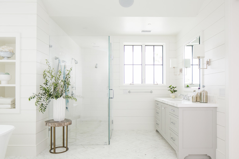 На фото: ванная комната в морском стиле с фасадами с утопленной филенкой, бежевыми фасадами, отдельно стоящей ванной, душем без бортиков, белыми стенами, врезной раковиной, белым полом и душем с распашными дверями с