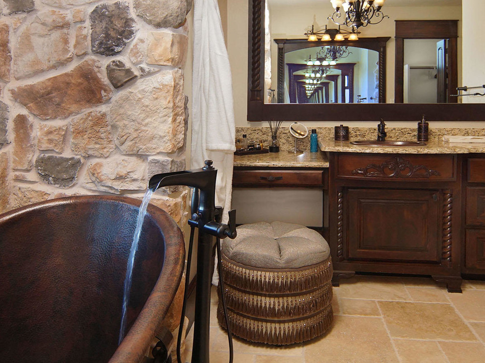 Exemple d'une grande douche en alcôve principale méditerranéenne en bois foncé avec un placard avec porte à panneau surélevé, une baignoire indépendante, un carrelage beige, un carrelage de pierre, un mur beige, un sol en carrelage de céramique, un lavabo encastré et un plan de toilette en granite.