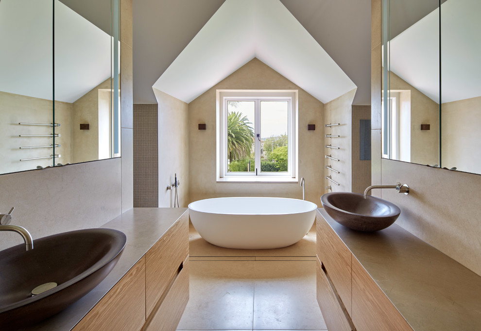 На фото: ванная комната среднего размера в современном стиле с настольной раковиной, плоскими фасадами, фасадами цвета дерева среднего тона, отдельно стоящей ванной и бежевыми стенами с