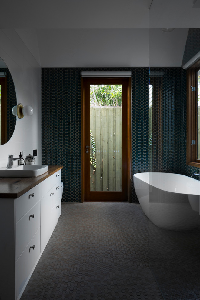 Bild på ett funkis en-suite badrum, med ett fristående badkar, en hörndusch, en toalettstol med separat cisternkåpa, grön kakel, mosaik, gröna väggar, mosaikgolv, ett nedsänkt handfat, träbänkskiva, flerfärgat golv och med dusch som är öppen
