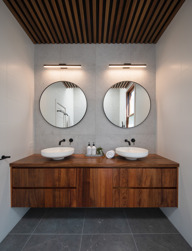 На фото: ванная комната в современном стиле с плоскими фасадами, темными деревянными фасадами, настольной раковиной, столешницей из дерева, серым полом, коричневой столешницей и тумбой под две раковины