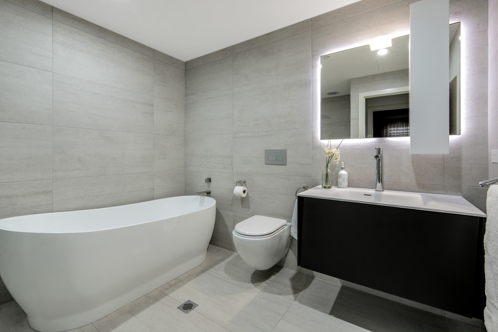 Medium sized modern bathroom in Melbourne with raised-panel cabinets, black cabinets, a freestanding bath, a one-piece toilet, ceramic tiles, ceramic flooring, an integrated sink and solid surface worktops.