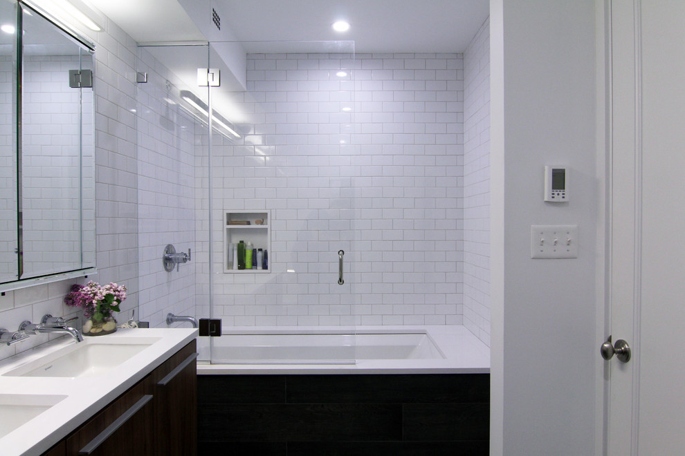 Aménagement d'une salle de bain principale moderne en bois foncé de taille moyenne avec un lavabo encastré, un combiné douche/baignoire, un carrelage blanc, un mur blanc, WC suspendus, des carreaux de céramique, un sol en carrelage de porcelaine, un placard à porte plane, un plan de toilette en quartz et une baignoire encastrée.