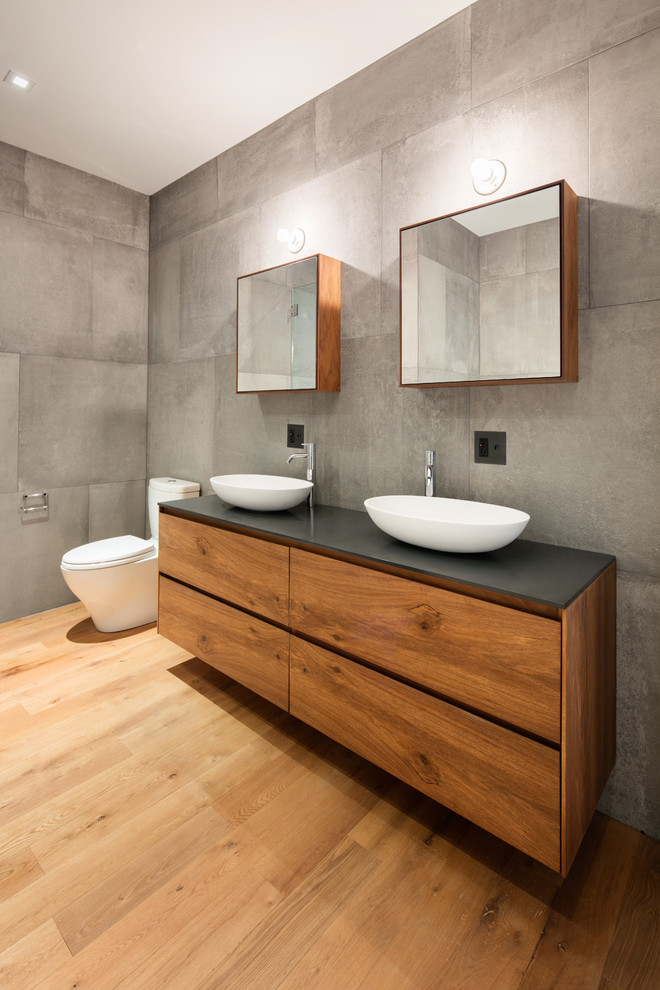 Inspiration pour une salle d'eau design en bois brun avec un placard à porte plane, un carrelage gris, des carreaux de béton, un mur gris, un sol en bois brun, une vasque et un sol marron.