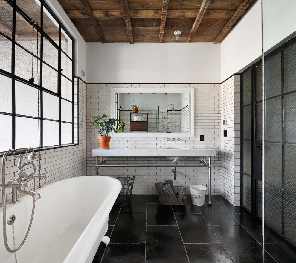 Exemple d'une salle d'eau industrielle de taille moyenne avec une baignoire posée, WC séparés, un carrelage blanc, un carrelage métro, un mur blanc, un lavabo encastré, un sol noir et un plan de toilette blanc.