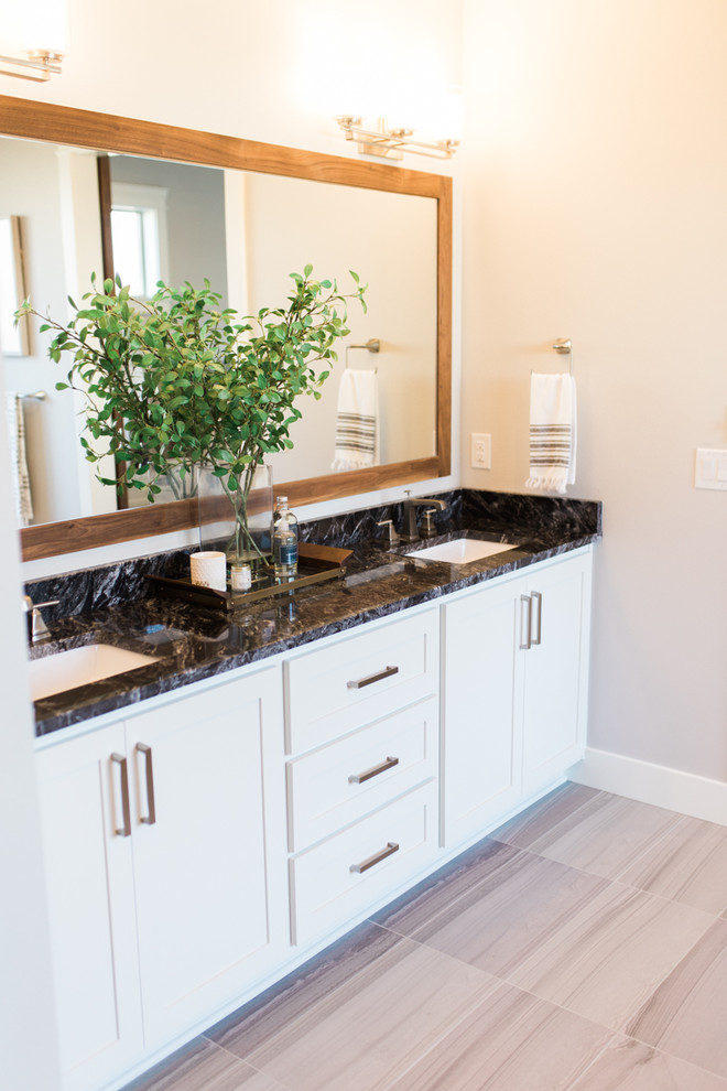 Photo of a large classic ensuite bathroom in Portland with shaker cabinets, white cabinets, a freestanding bath, a walk-in shower, a one-piece toilet, white tiles, ceramic tiles, grey walls, ceramic flooring, a built-in sink, granite worktops, grey floors, a hinged door and black worktops.