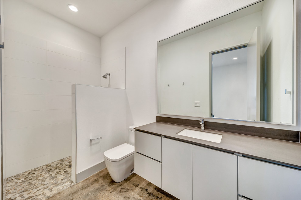 Inredning av ett modernt mellanstort badrum med dusch, med släta luckor, vita skåp, en dusch i en alkov, en toalettstol med hel cisternkåpa, vit kakel, porslinskakel, vita väggar, betonggolv, ett undermonterad handfat, bänkskiva i akrylsten, brunt golv och med dusch som är öppen
