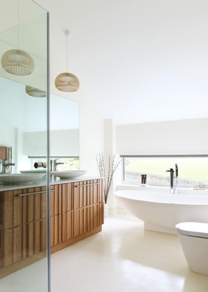 Inspiration for a large contemporary ensuite bathroom in Oxfordshire with medium wood cabinets, a freestanding bath, a one-piece toilet, white walls, a vessel sink, beige floors, grey worktops, double sinks, a built in vanity unit and flat-panel cabinets.