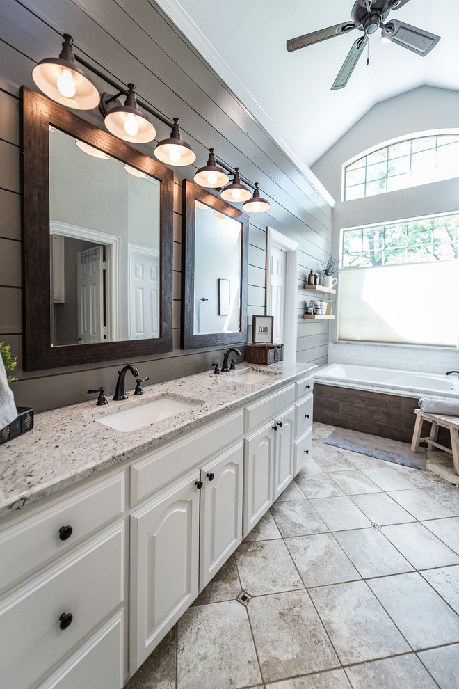 This is an example of a medium sized farmhouse ensuite bathroom in Dallas with raised-panel cabinets, white cabinets, a built-in bath, an alcove shower, grey tiles, ceramic tiles, grey walls, travertine flooring, a submerged sink, granite worktops, beige floors and a hinged door.