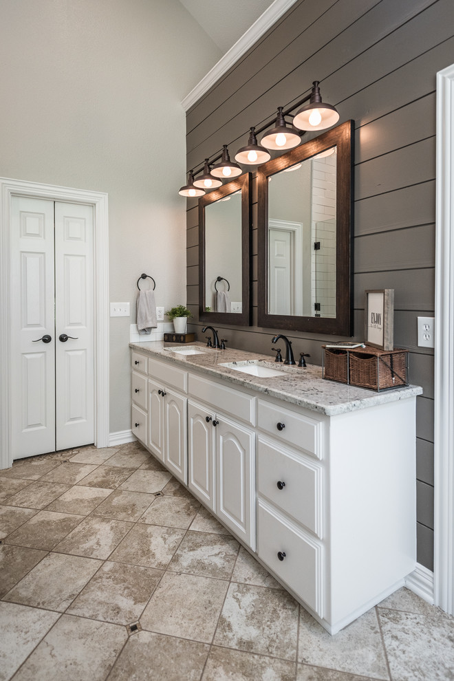 Photo of a medium sized farmhouse ensuite bathroom in Dallas with raised-panel cabinets, white cabinets, a built-in bath, an alcove shower, grey tiles, ceramic tiles, grey walls, travertine flooring, a submerged sink, granite worktops, beige floors and a hinged door.