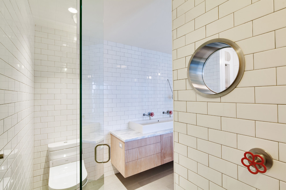 This is an example of a medium sized urban ensuite bathroom in Vancouver with flat-panel cabinets, light wood cabinets, a claw-foot bath, a one-piece toilet, metro tiles, white walls, limestone flooring, a vessel sink and marble worktops.