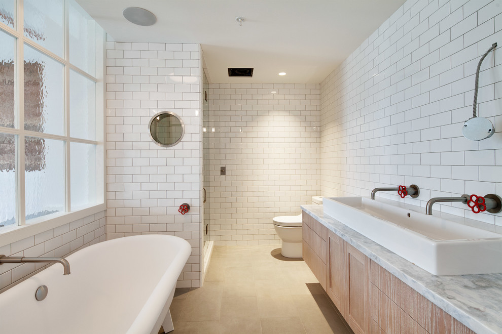 Inspiration for a mid-sized industrial master subway tile limestone floor claw-foot bathtub remodel in Vancouver with flat-panel cabinets, light wood cabinets, a one-piece toilet, white walls, a vessel sink and marble countertops