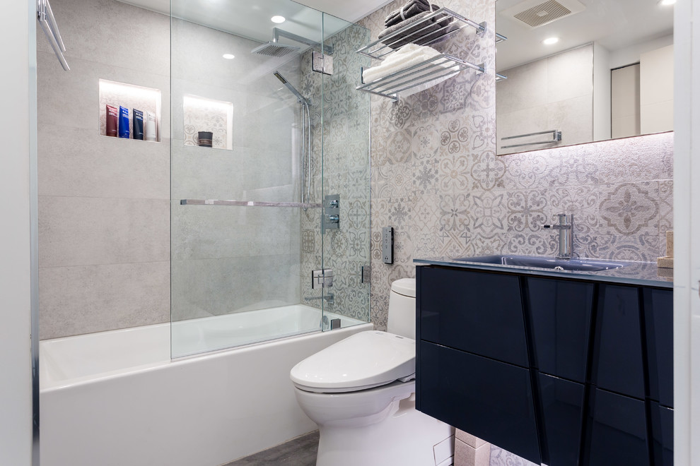 На фото: ванная комната среднего размера в современном стиле с плоскими фасадами, черными фасадами, ванной в нише, душем над ванной, унитазом-моноблоком, серой плиткой, керамогранитной плиткой, серыми стенами, полом из цементной плитки, душевой кабиной, монолитной раковиной, стеклянной столешницей, серым полом, душем с распашными дверями и синей столешницей с