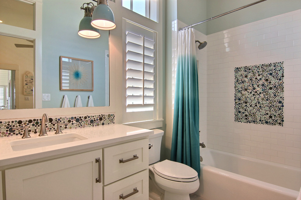 Cette image montre une salle de bain marine de taille moyenne avec un placard à porte shaker, des portes de placard blanches, une baignoire posée, un combiné douche/baignoire, WC à poser, un carrelage blanc, des carreaux de porcelaine, un mur bleu, un sol en carrelage de porcelaine, un lavabo encastré, un plan de toilette en quartz, un sol blanc et une cabine de douche avec un rideau.