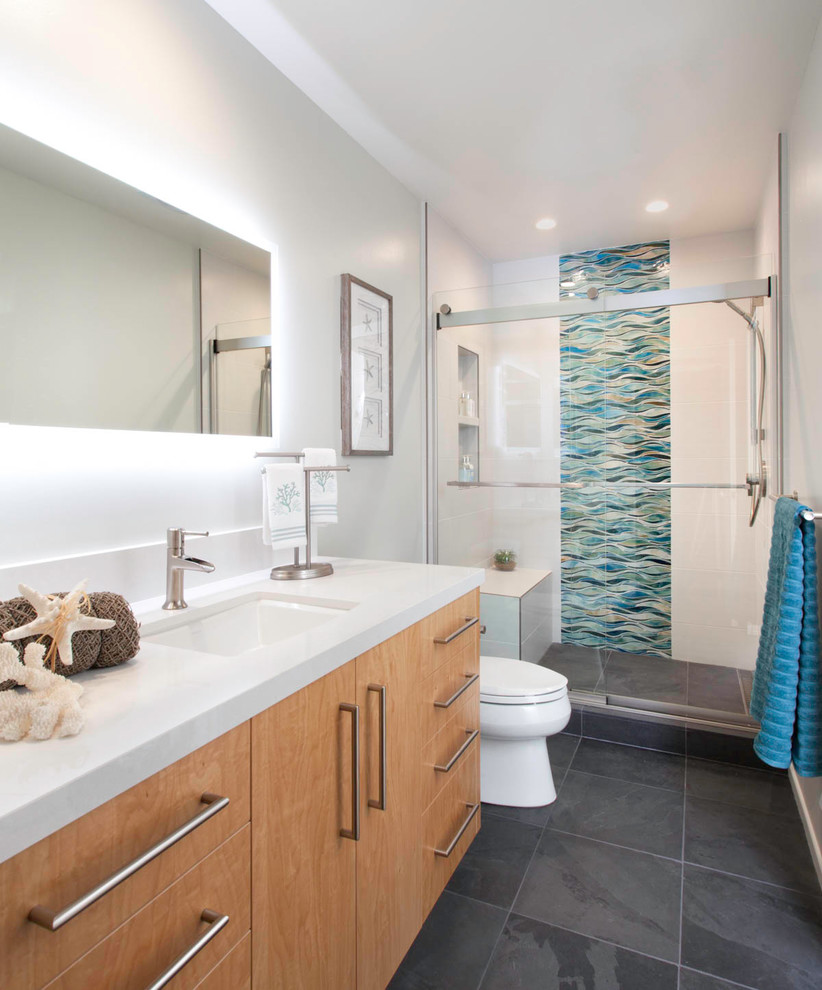 Maritimes Badezimmer mit flächenbündigen Schrankfronten, hellbraunen Holzschränken, Duschnische, farbigen Fliesen, weißer Wandfarbe, Unterbauwaschbecken, grauem Boden, Schiebetür-Duschabtrennung und weißer Waschtischplatte in San Diego