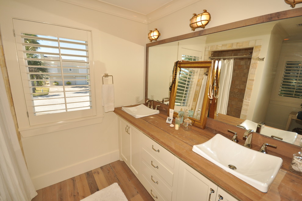 Modelo de cuarto de baño principal marinero pequeño con puertas de armario blancas, paredes blancas, suelo de madera clara y encimera de madera
