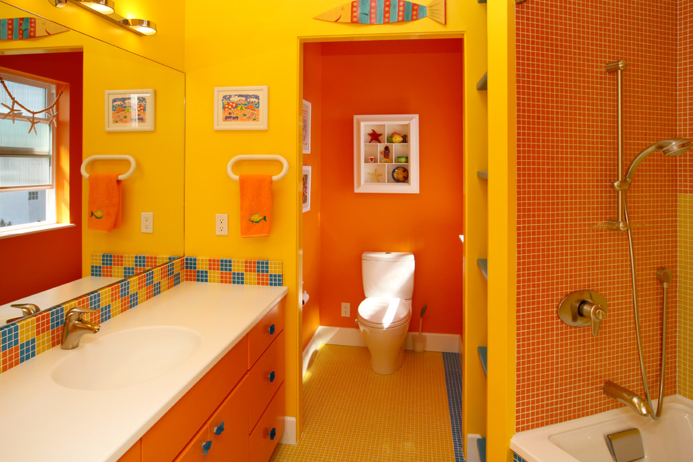 サンフランシスコにあるコンテンポラリースタイルのおしゃれな浴室 (オーバーカウンターシンク、フラットパネル扉のキャビネット、オレンジのキャビネット、ドロップイン型浴槽、シャワー付き浴槽	、一体型トイレ	、オレンジのタイル、モザイクタイル、黄色い壁、モザイクタイル) の写真
