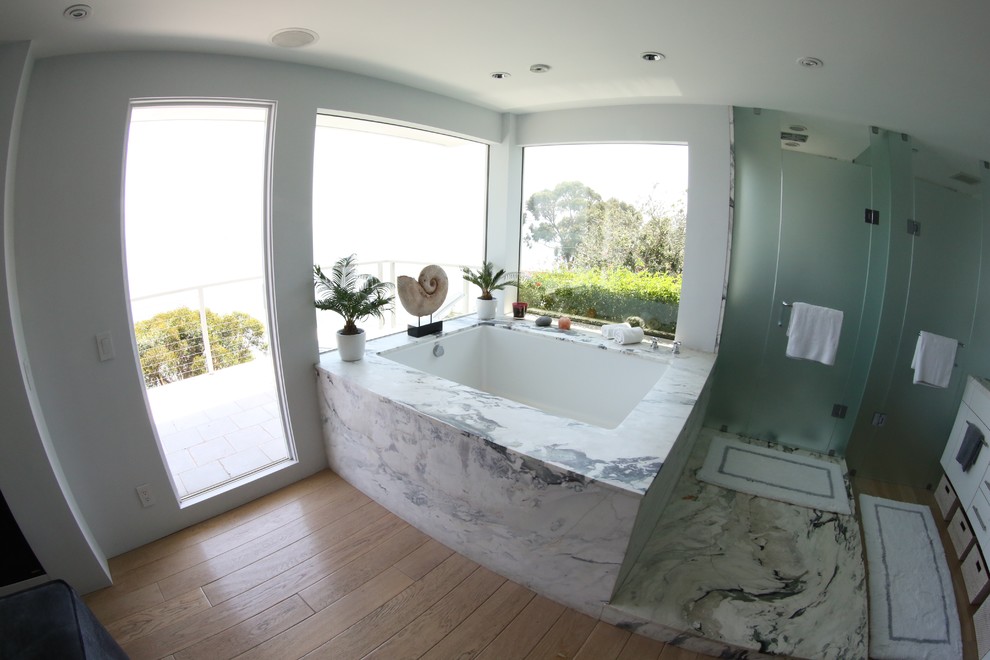 Cette image montre une salle de bain principale traditionnelle de taille moyenne avec un placard à porte plane, des portes de placard blanches, une baignoire d'angle, une douche double, du carrelage en marbre, un mur blanc et parquet clair.