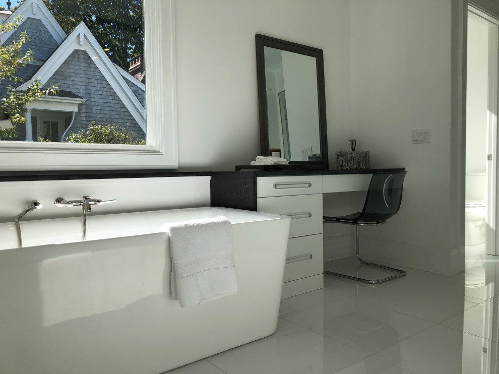 Aménagement d'une salle de bain principale moderne de taille moyenne avec des portes de placard blanches, une baignoire indépendante, WC séparés, un mur blanc, un sol en carrelage de porcelaine, un lavabo encastré, un sol gris et un plan de toilette noir.