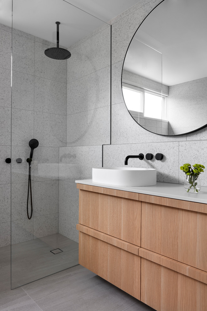 Photo of a medium sized coastal ensuite bathroom in Melbourne with recessed-panel cabinets, light wood cabinets, a freestanding bath, a walk-in shower, grey tiles, stone tiles, a vessel sink, concrete worktops, grey floors, a hinged door and white worktops.