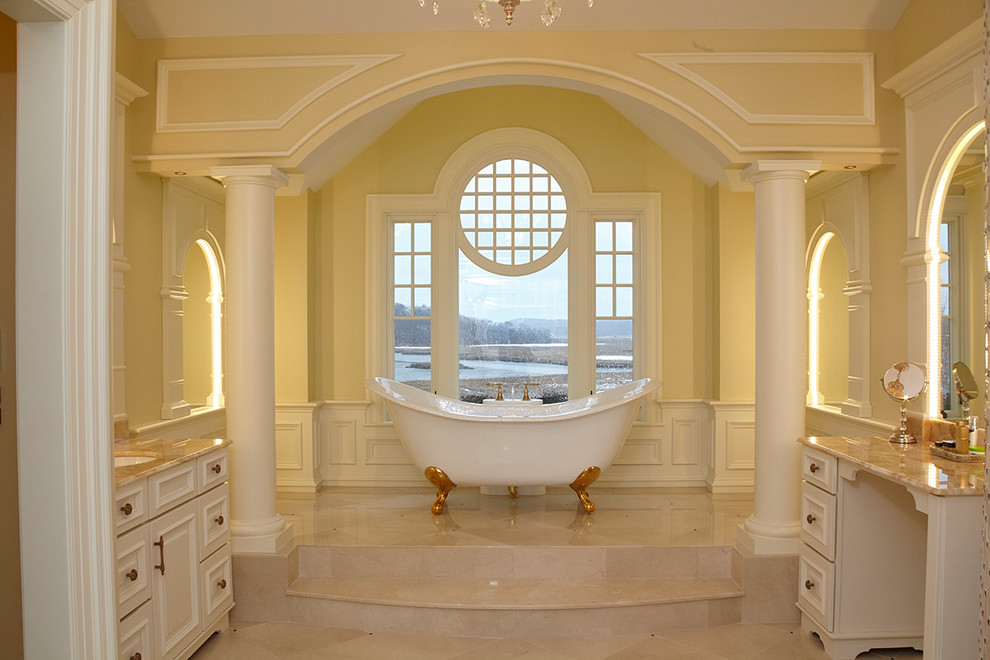 Стильный дизайн: огромная главная ванная комната в классическом стиле с фасадами с выступающей филенкой, бежевыми фасадами, ванной на ножках, угловым душем, унитазом-моноблоком, бежевой плиткой, мраморной плиткой, желтыми стенами, мраморным полом, врезной раковиной, столешницей из оникса, бежевым полом и открытым душем - последний тренд
