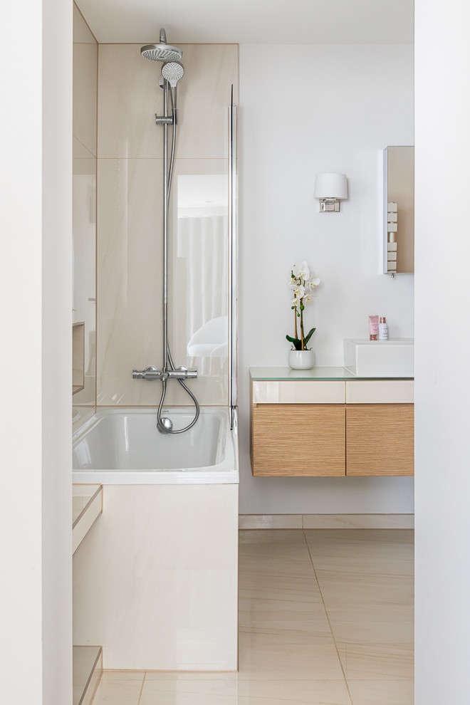 This is an example of a medium sized contemporary bathroom in Essex with flat-panel cabinets, beige cabinets, a built-in bath, a shower/bath combination, beige tiles, ceramic tiles and glass worktops.