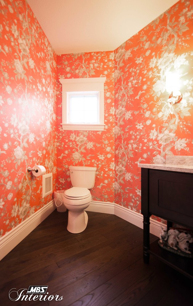Cette image montre un grand WC et toilettes traditionnel en bois foncé avec un placard à porte shaker, WC à poser, un mur orange, parquet foncé, un lavabo encastré, un plan de toilette en granite et un sol marron.