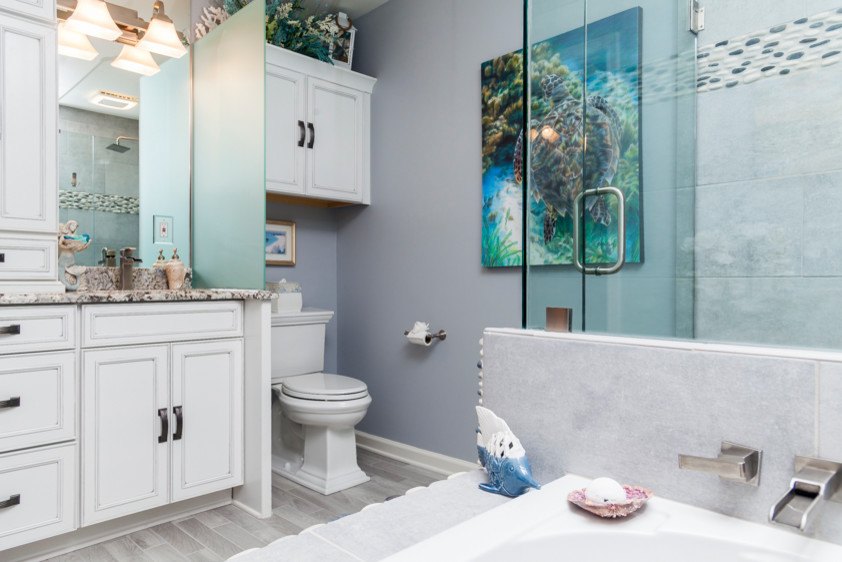 Idées déco pour une petite salle de bain principale bord de mer avec un placard avec porte à panneau encastré, une baignoire posée, un mur bleu, un sol en carrelage de porcelaine, un lavabo encastré, un plan de toilette en granite et un sol gris.