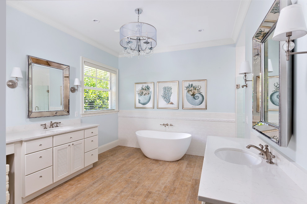 Design ideas for a coastal ensuite bathroom in Miami with flat-panel cabinets, white cabinets, a freestanding bath, blue walls, light hardwood flooring and a submerged sink.