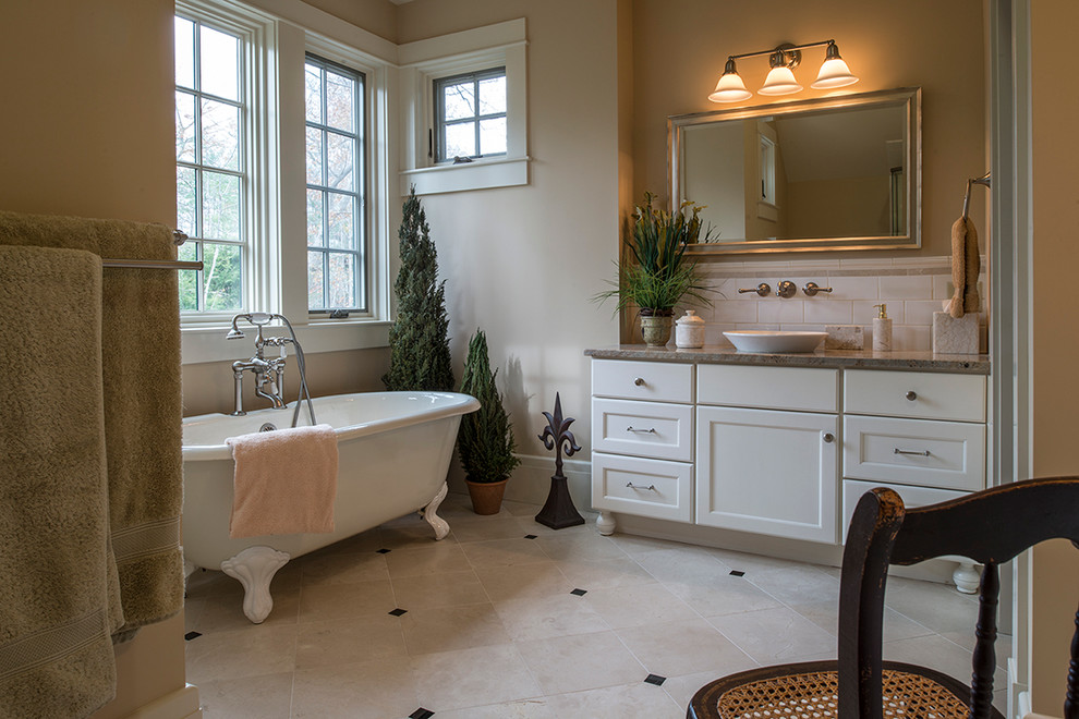 Aménagement d'une grande salle de bain principale classique avec une baignoire sur pieds, un placard à porte shaker, un plan de toilette en granite, une vasque, des portes de placard blanches et un mur beige.