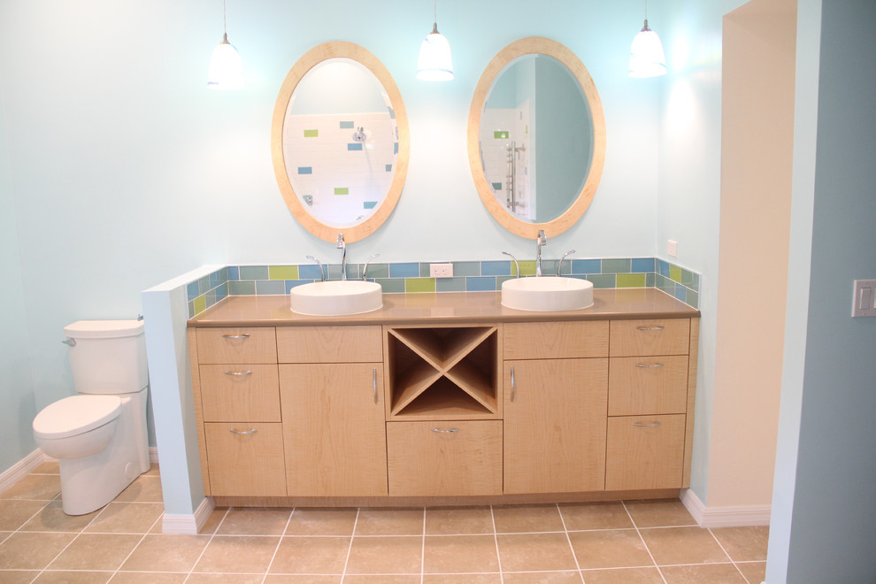 Example of a mid-sized beach style master multicolored tile and glass tile ceramic tile and beige floor bathroom design in Miami with flat-panel cabinets, light wood cabinets, a two-piece toilet, blue walls, a vessel sink and quartz countertops