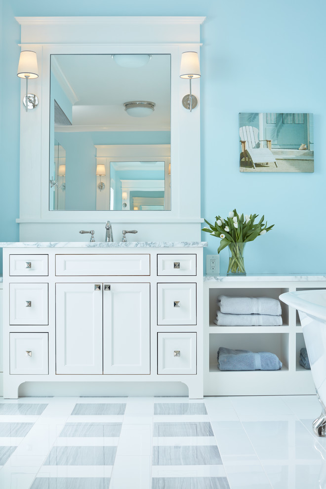 Foto de cuarto de baño principal, costero, con armarios tipo mueble, puertas de armario blancas, bañera exenta, baldosas y/o azulejos blancos, paredes azules, suelo de baldosas de cerámica, lavabo encastrado y encimera de granito