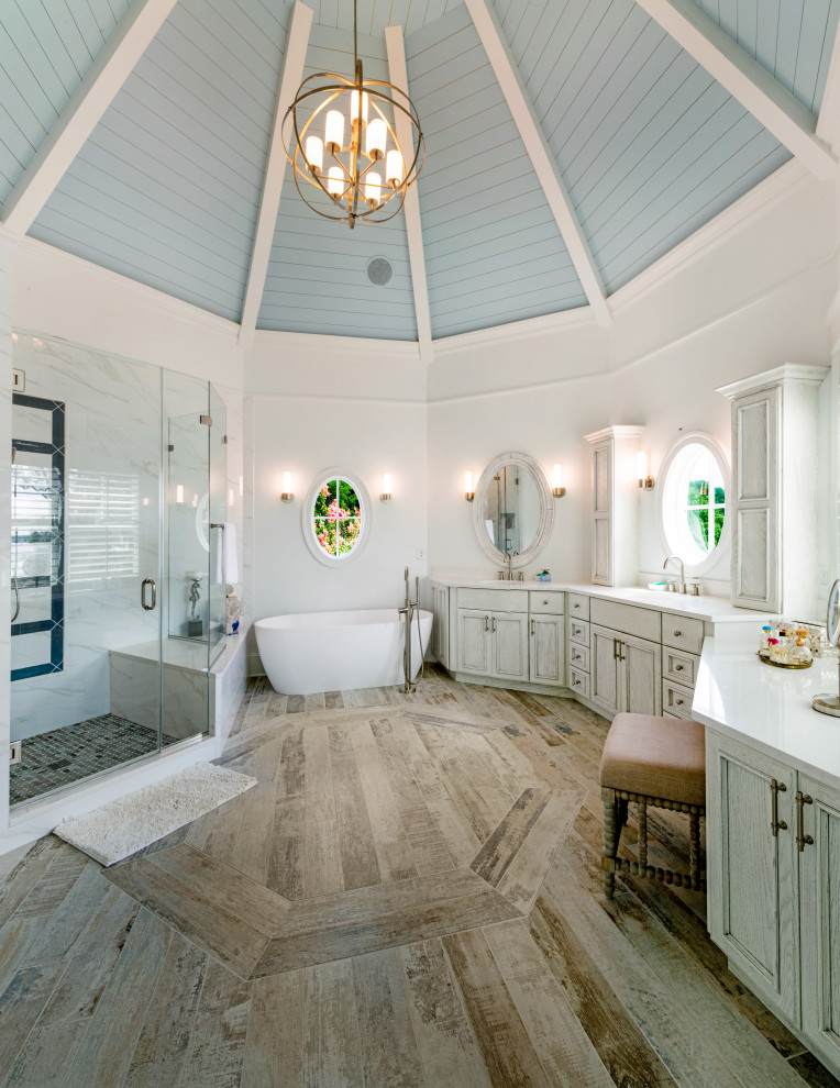 Exemple d'une salle de bain principale bord de mer avec un placard avec porte à panneau encastré, des portes de placard grises, une baignoire indépendante, une douche d'angle, un mur blanc, un sol en bois brun, un lavabo encastré, un sol marron, une cabine de douche à porte battante, un plan de toilette blanc, un banc de douche, meuble double vasque, meuble-lavabo encastré, poutres apparentes, un plafond en lambris de bois et un plafond voûté.