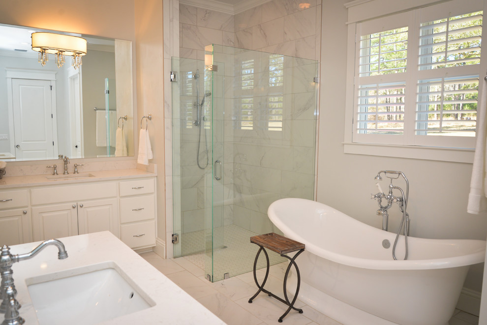 Lantlig inredning av ett stort en-suite badrum, med luckor med upphöjd panel, vita skåp, ett fristående badkar, en kantlös dusch, en toalettstol med separat cisternkåpa, vit kakel, grå kakel, ett undermonterad handfat, stenkakel, vita väggar, marmorgolv och marmorbänkskiva