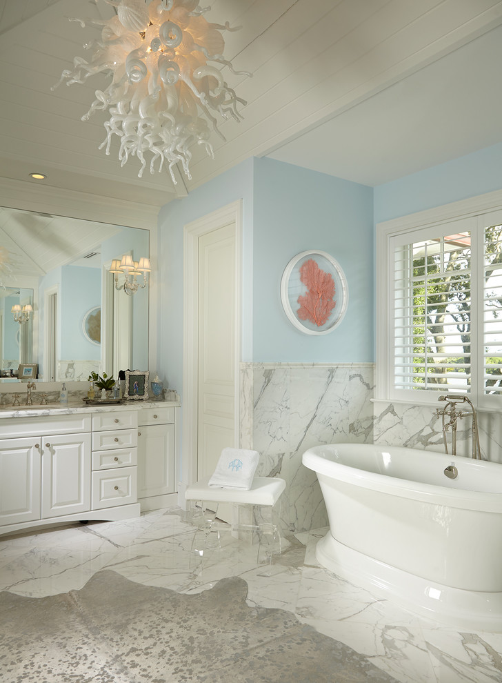 Beach style bathroom in Miami with raised-panel cabinets, white cabinets, a freestanding bath, white tiles, blue walls, white floors and white worktops.