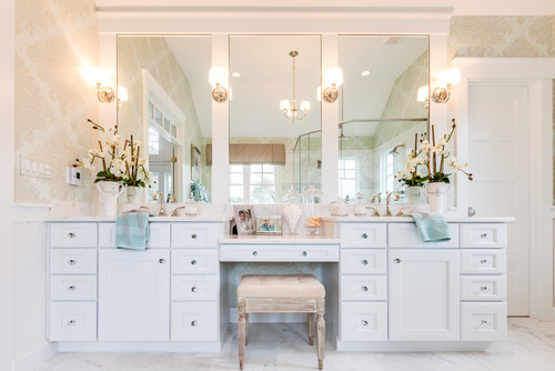 Bright bathroom with white double vanities, built-in makeup desk, large mirrors, and decorative lighting