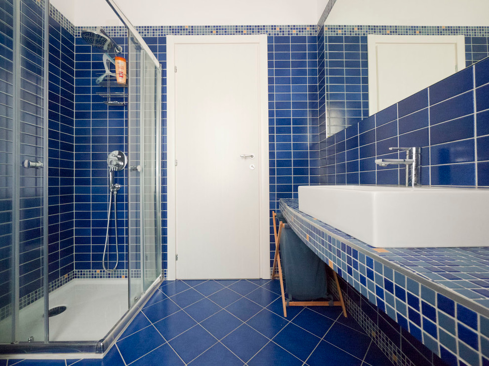 This is an example of a small mediterranean ensuite bathroom in Milan with a console sink, tiled worktops, a corner shower, a wall mounted toilet, blue tiles, porcelain tiles, blue walls and porcelain flooring.