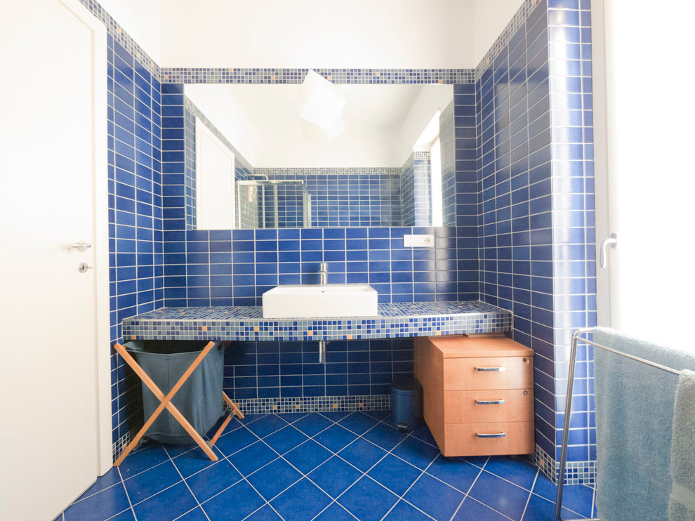 Inspiration för små medelhavsstil en-suite badrum, med ett konsol handfat, kaklad bänkskiva, en hörndusch, en vägghängd toalettstol, blå kakel, porslinskakel, blå väggar och klinkergolv i porslin
