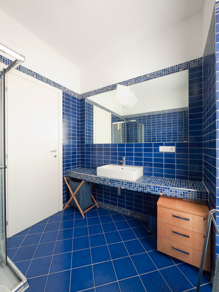 Idéer för små medelhavsstil en-suite badrum, med ett konsol handfat, kaklad bänkskiva, en hörndusch, en vägghängd toalettstol, blå kakel, porslinskakel, blå väggar och klinkergolv i porslin