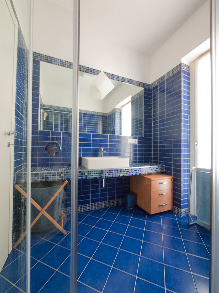 Corner shower - small mediterranean master blue tile and porcelain tile porcelain tile corner shower idea in Milan with a console sink, tile countertops, a wall-mount toilet and blue walls