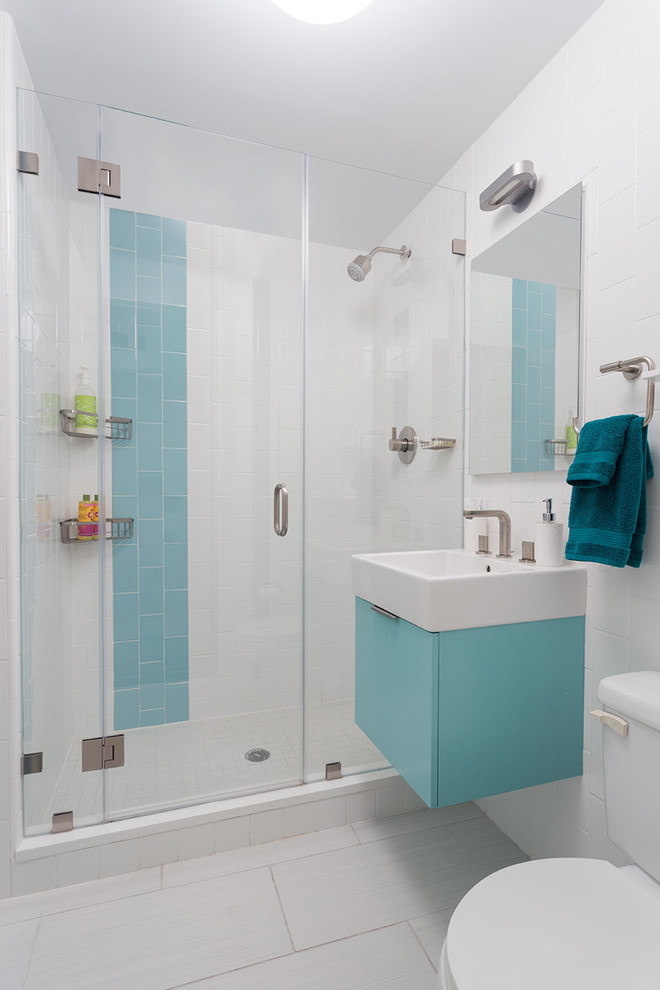 Modern inredning av ett litet badrum för barn, med ett väggmonterat handfat, släta luckor, blå skåp, en toalettstol med separat cisternkåpa, flerfärgad kakel, keramikplattor, vita väggar, klinkergolv i keramik och en dusch i en alkov