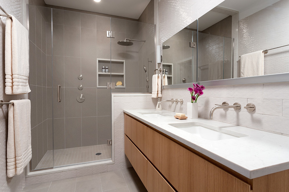 Modern inredning av ett en-suite badrum, med ett undermonterad handfat, släta luckor, skåp i ljust trä, bänkskiva i kvarts, beige kakel, keramikplattor, vita väggar och klinkergolv i keramik