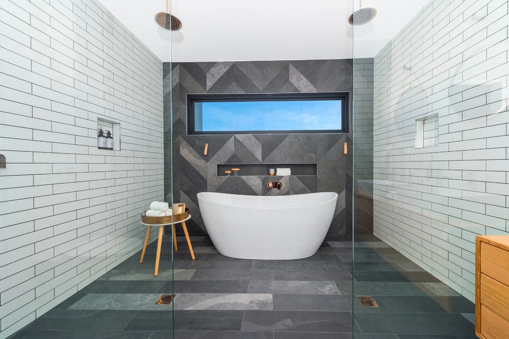 Large contemporary ensuite bathroom in Melbourne with beaded cabinets, light wood cabinets, a freestanding bath, a double shower, a wall mounted toilet, grey tiles, metro tiles, white walls, ceramic flooring, a vessel sink and solid surface worktops.