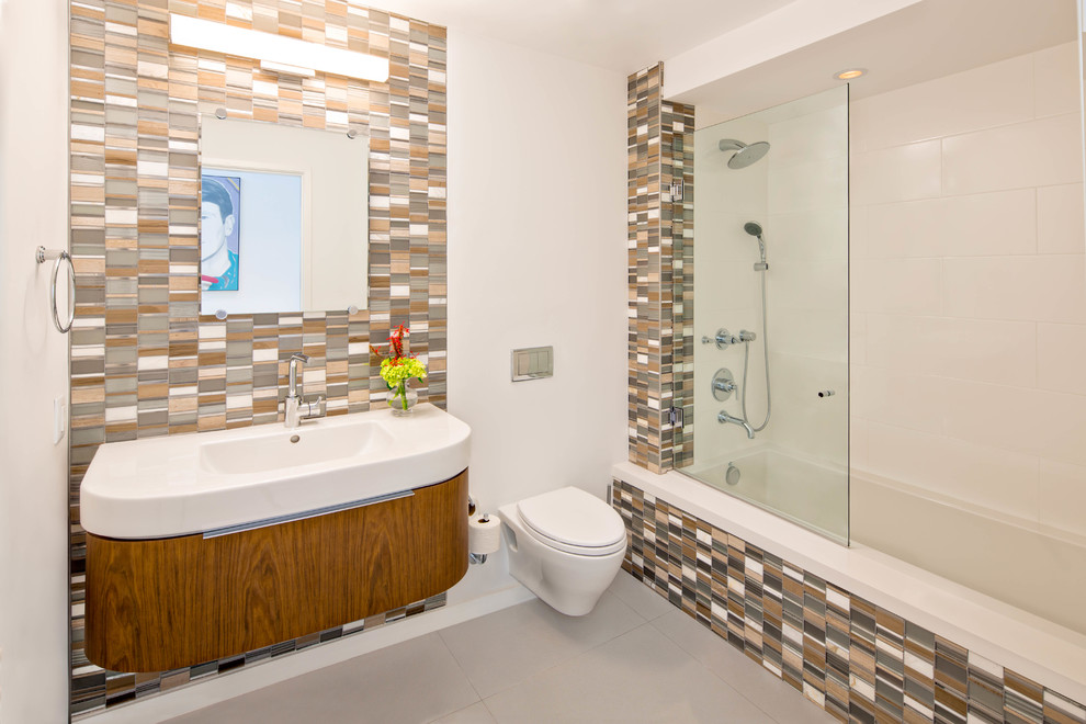Inspiration for a mid-sized modern 3/4 multicolored tile and glass tile porcelain tile drop-in bathtub remodel in Miami with an integrated sink, flat-panel cabinets, medium tone wood cabinets, a wall-mount toilet and white walls