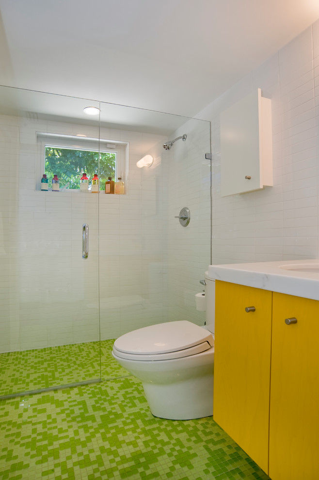 Kleines Modernes Duschbad mit Unterbauwaschbecken, flächenbündigen Schrankfronten, gelben Schränken, Marmor-Waschbecken/Waschtisch, bodengleicher Dusche, Wandtoilette mit Spülkasten, grünen Fliesen, Glasfliesen, weißer Wandfarbe und Mosaik-Bodenfliesen in Miami
