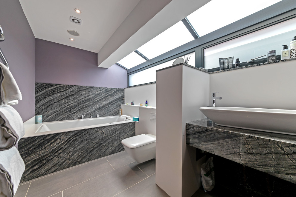 На фото: ванная комната среднего размера в современном стиле с плоскими фасадами, черными фасадами, ванной в нише, душем над ванной, фиолетовыми стенами, настольной раковиной, мраморной столешницей, серым полом и черной столешницей с