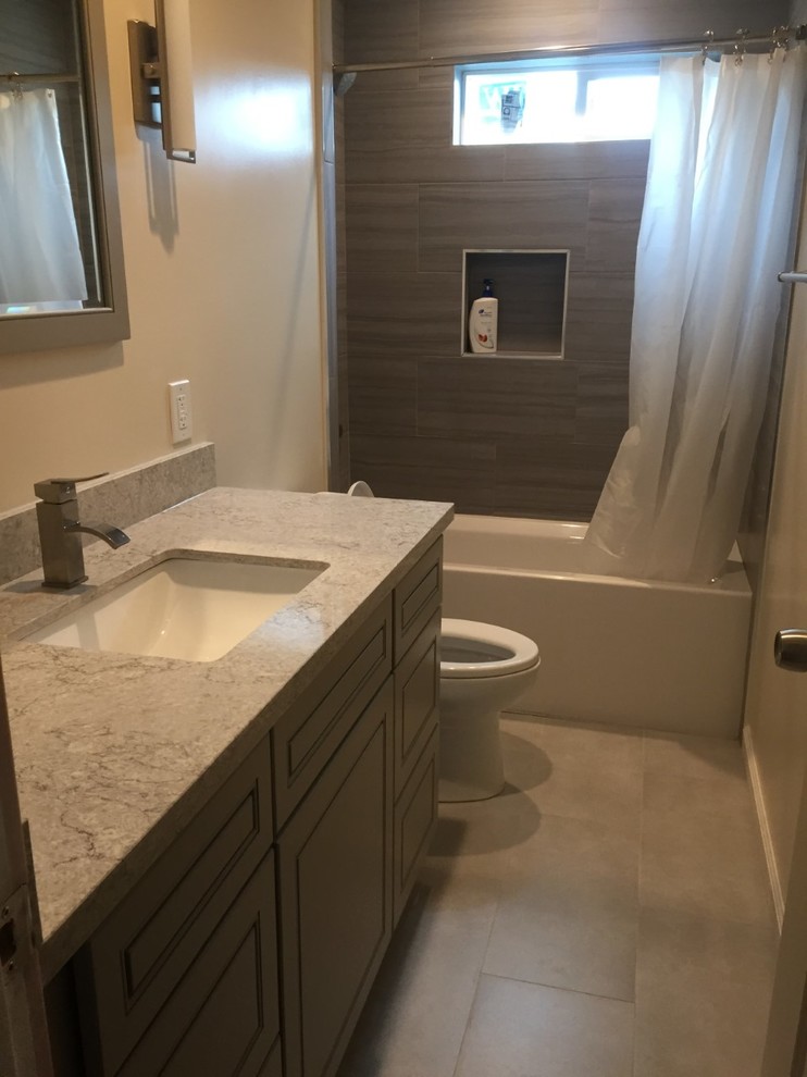 Cette photo montre une salle de bain principale tendance de taille moyenne avec un placard avec porte à panneau surélevé, des portes de placard grises, une baignoire posée, un combiné douche/baignoire, WC à poser, un carrelage gris, des carreaux de céramique, un mur blanc, un sol en ardoise, un lavabo encastré, un plan de toilette en granite, un sol blanc, une cabine de douche avec un rideau et un plan de toilette gris.