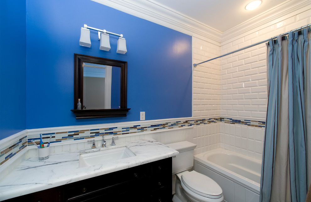 Idee per una stanza da bagno con doccia classica di medie dimensioni con lavabo sottopiano, ante con riquadro incassato, ante in legno bruno, top in marmo, vasca da incasso, vasca/doccia, WC a due pezzi, piastrelle bianche, piastrelle in ceramica, pareti blu e parquet scuro