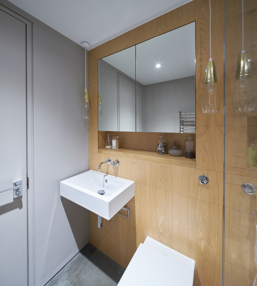 Photo of a large ensuite bathroom in London with flat-panel cabinets, light wood cabinets, a double shower, a wall mounted toilet, grey walls, concrete flooring, a wall-mounted sink and wooden worktops.