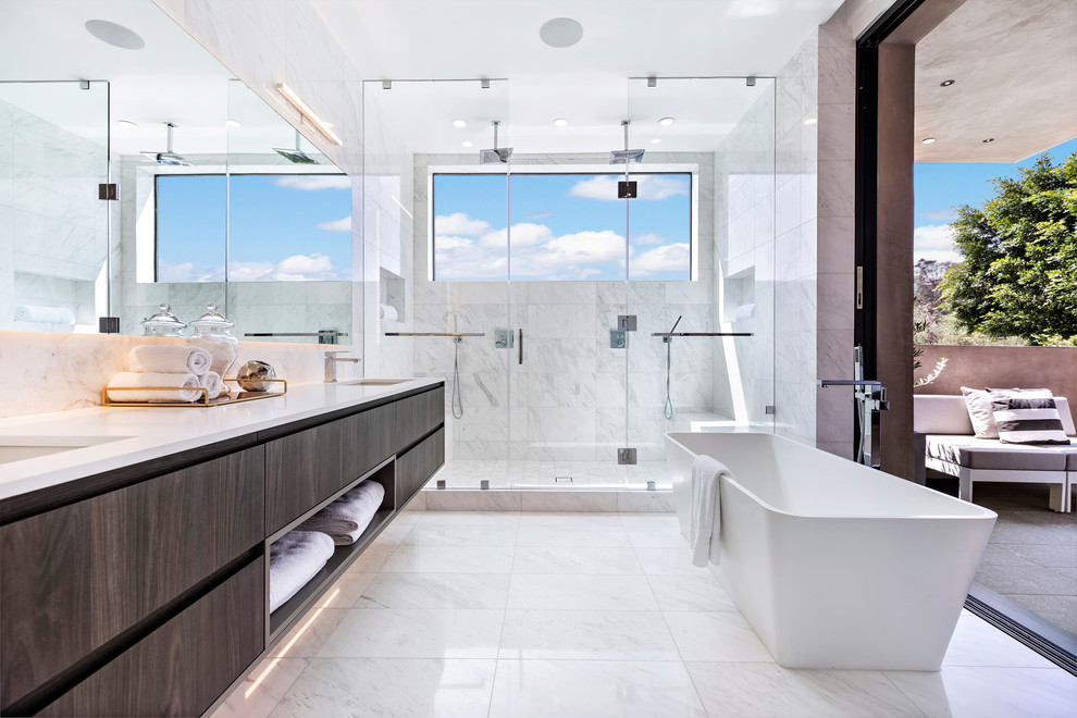 Bild på ett funkis vit vitt en-suite badrum, med släta luckor, bruna skåp, ett fristående badkar, en dubbeldusch, grå kakel, grå väggar, ett väggmonterat handfat, grått golv och med dusch som är öppen